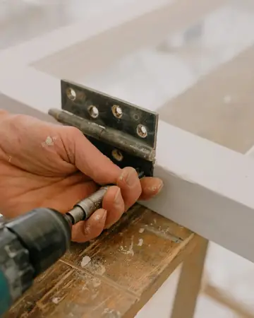 A handyman fitting a hinge with a drill
